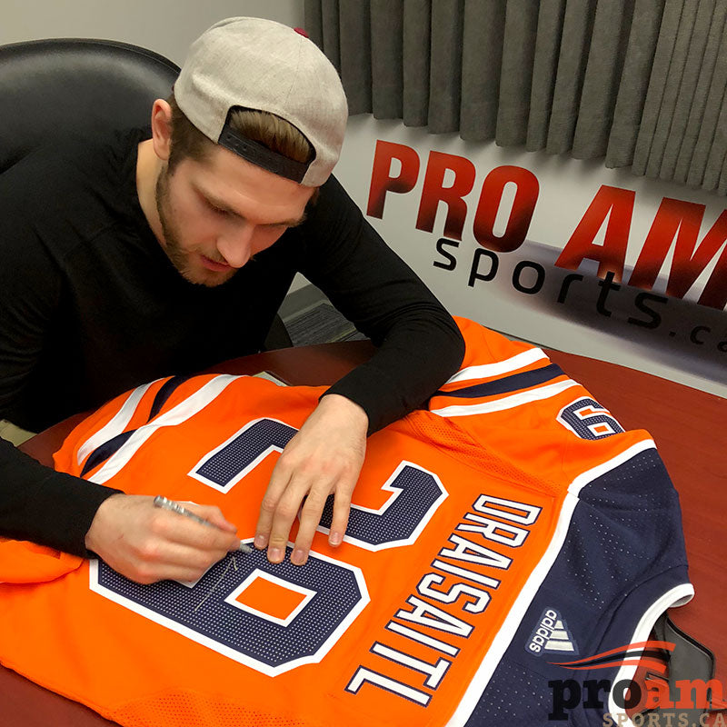 Leon Draisaitl signing an orange Edmonton Oilers NHL home jersey during a signing at Pro Am Sports in Edmonton