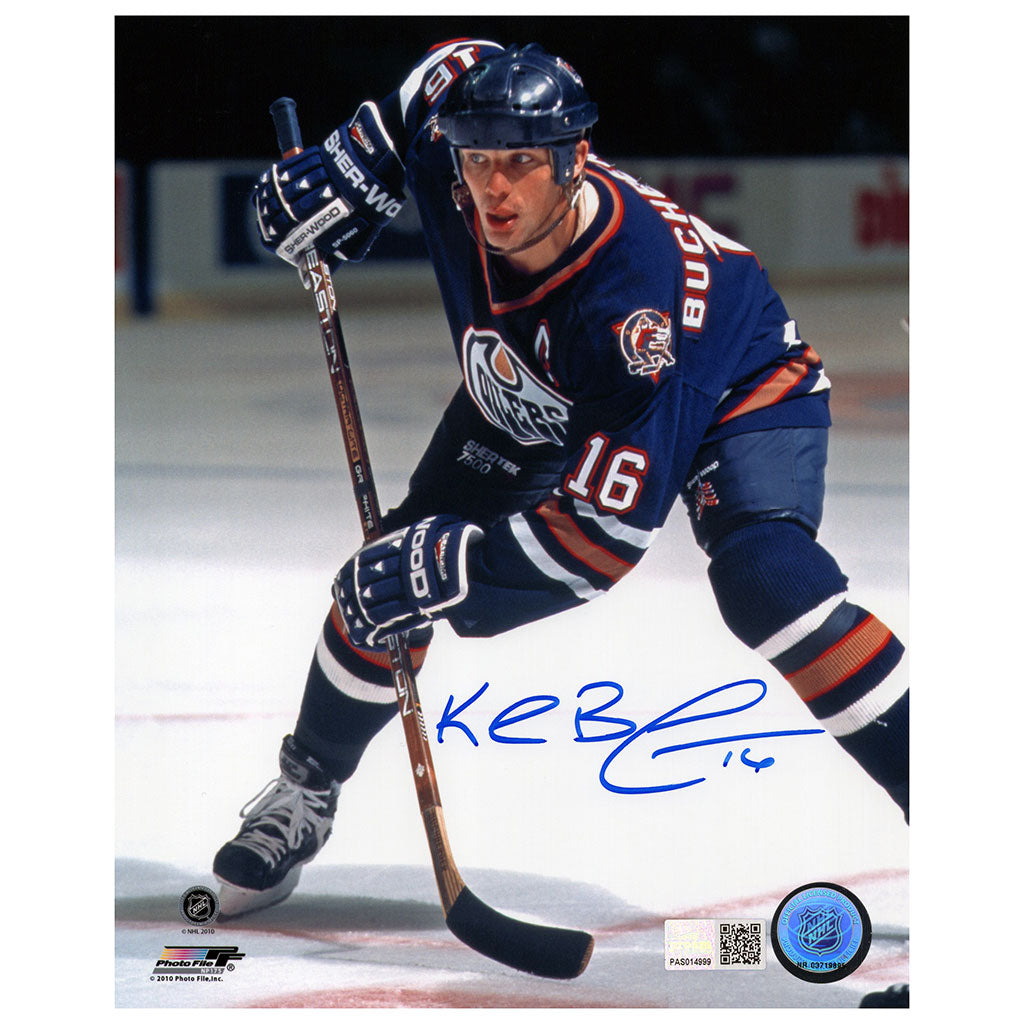An autographed 8x10 photograph of hockey player Kevin Buchberger (number 16) in a dark blue Edmonton Oilers uniform, signed in blue ink across the lower center. The photo includes a physical authentication sticker in the bottom right corner.