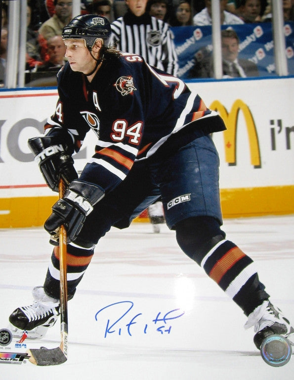 Ryan Smyth skating during an Edmonton Oilers game, wearing Oilers Oil Man jersey. Photo is signed by Smyth in blue ink in the bottom centre of the photo.