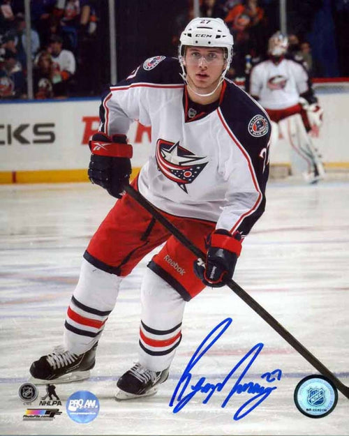 Ryan Murray of the Columbus Blue Jackets skating with hockey stick during an NHL hockey game. He is wearing white jersey with red shorts. He is looking directly at the camera. Photo is signed by Murray in blue ink in the bottom right corner. 