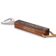 Bottle opener made from wooden seat from Notre Dame Stadium. The wood handle has been cut and trimmed, then embosses with white text reading "Made of seat from Notre Dame Stadium". Bottle opener is made from silver metal; there is a gold cord for handing on the end of the handle. Bottle opener is pictured on a white background.