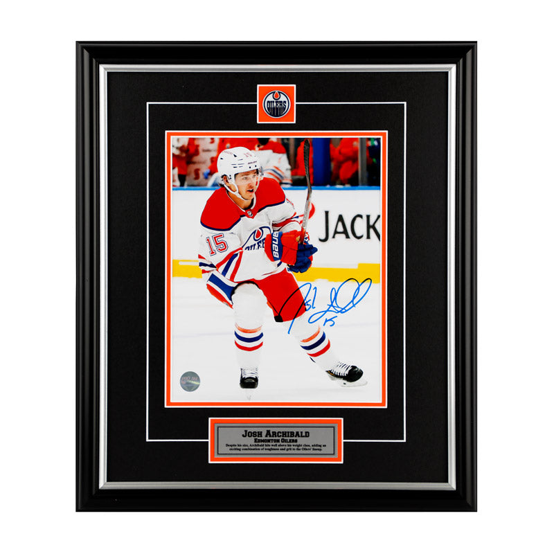 Photo of Edmonton Oilers Josh Archibald skating during an Oilers NHL hockey game, he is wearing white jersey. Photo is signed in blue ink in the lower right. Photo is shown framed, with black framing and mat with orange accents and inset team pin and description plate.