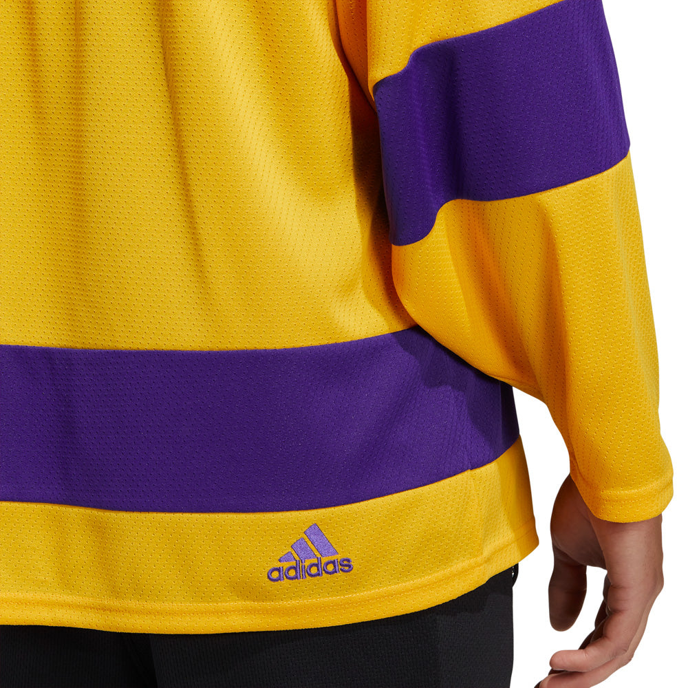 Front view of adidas Vintage team classics 1967 Los Angeles Kings jersey, featuringpurple bands on sleeves and lower hem, and purple collar. Primary jersey collar is a bright sunshine yellow. Small embroidered adidas logo on lower right hem shown in detail