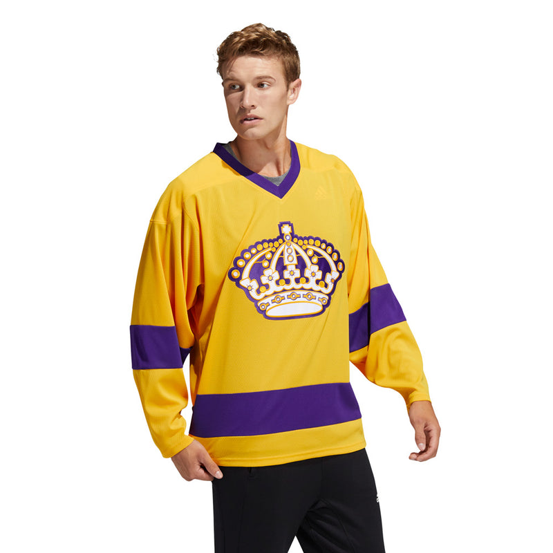 Model wearing the adidas vintage team classis Los Angeles Kings jersey. He is walking and looking to the left. the jersey is bright yellow and purple with embroidered crown logo in front. 