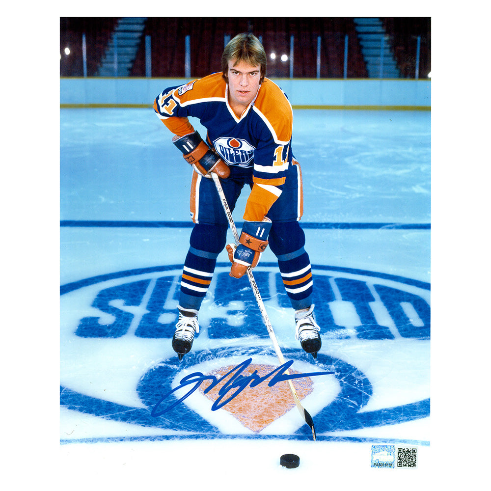 Signed photo of young Mark Messier posed on the ice with stick and puck. He is wearing the Edmonton Oilers royal blue jersey. Photo is signed near the bottom in blue ink.