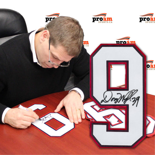 Photo of Doug Weight signing jersey numbers while seated at  a table, large signed number 9 is inset in the image 