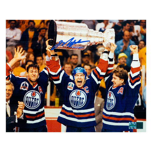 Signed photo of Mark Messier holding the Stanley Cup above his head in celebration of winning the 1990 championship. He is flanked by Kevin Lowe on the left and Jari Kurri on the right. Photo is signed in the top centre, on top of the Stanley Cup in blue ink. 