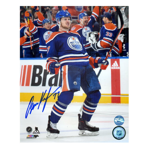 Photo of Oscar Klefbom celebrating during an Edmonton Oilers NHL hockey game. He is wearing the royal blue jersey. Photo is signed in the bottom left corner with blue ink