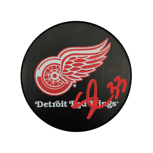 Black hockey puck with large Detroit Red Wings logo and text, puck is signed by Sebastian Cossa in red ink. 