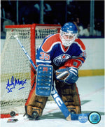 Andy Moog photographed guarding the net during an Edmonton Oilers NHL hockey game. Moog is wearing royal blue Oilers jersey with blue and brown pads. Photo is signed on the left side near the bottom in blue ink. 