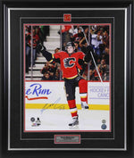 Sean Monahan celebrating during a Calgary Flames NHL hockey game. He is wearing red jersey with black shorts and helmet. Photo is signed by Monahan in the bottom left corner. Photo is shown framed with black frame, black mat with red accent, Calgary Flames team pin and description plate are inset. 