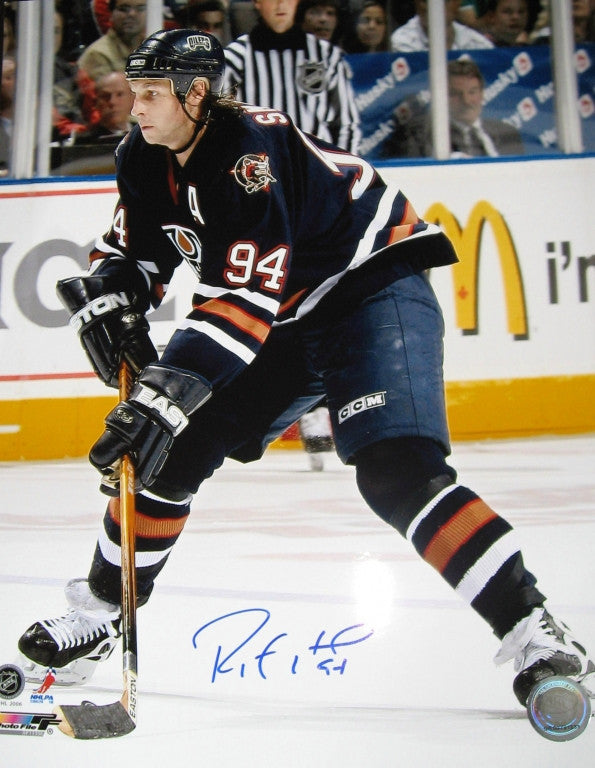 Ryan Smyth skating during an Edmonton Oilers game, wearing Oilers Oil Man jersey. Photo is signed by Smyth in blue ink in the bottom  centre of the photo. 