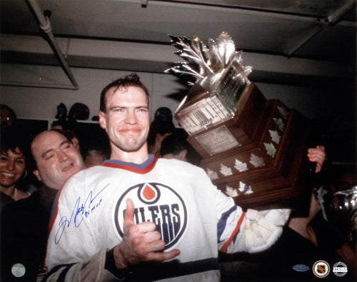 Mark Messier Edmonton Oilers holding the Conn Smyth trophy in 1984. He is wearing the white Oilers jersey and smiling. Photo is signed by Messier in blue ink on the lower left part of the photo, on the shoulder of his jersey. 