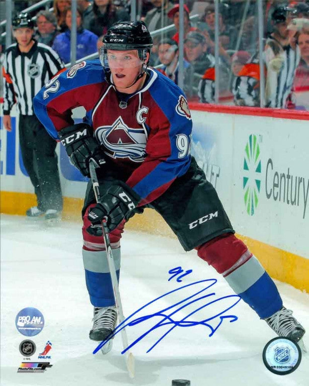 Gabriel Landeskog skating during a Colorado Avalanche NHL hockey game. He is wearing red and blue team jersey with captain's "C". Photo is signed by Landeskog with blue ink 