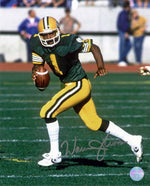 Warren Moon Edmonton Elks / Edmonton Football Team shown running with the ball, wearing green and gold uniform. Image is signed by Moon with silver in at the bottom of the photo. 