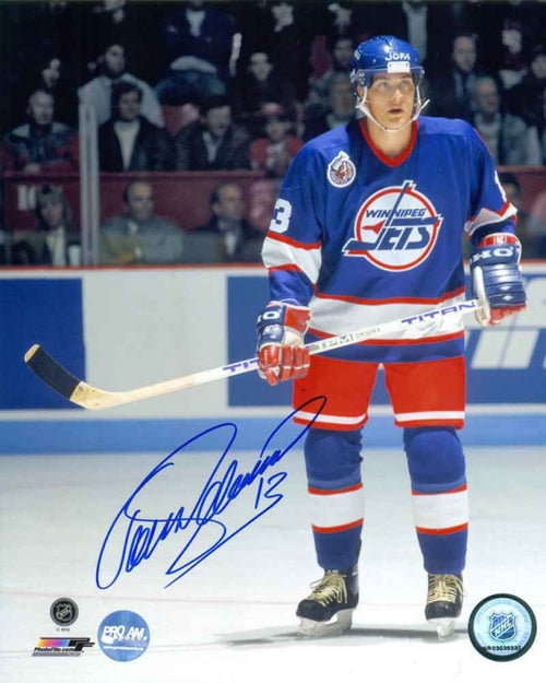 Teemu Selanne during a Winnipeg Jets NHL hockey game, he is wearing blue Jets jersey and is stationery on the ice, holding his stick and watching down ice. Photo is signed by Selanne in blue ink in the bottom left. 