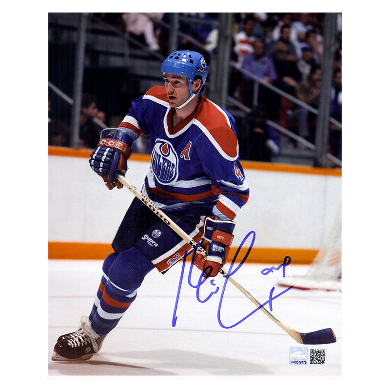 Action photo of Edmonton Oiler Kevin Lowe skating during an NHL game. He is wearing the Oilers royal blue jersey with alternate captain's "A" on chest. Photo is signed by Lowe on the lower right side in blue ink 