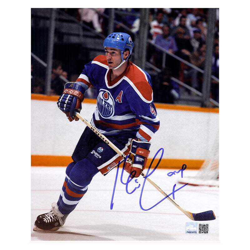 Action photo of Edmonton Oiler Kevin Lowe skating during an NHL game. He is wearing the Oilers royal blue jersey with alternate captain's "A" on chest. Photo is signed by Lowe on the lower right side in blue ink