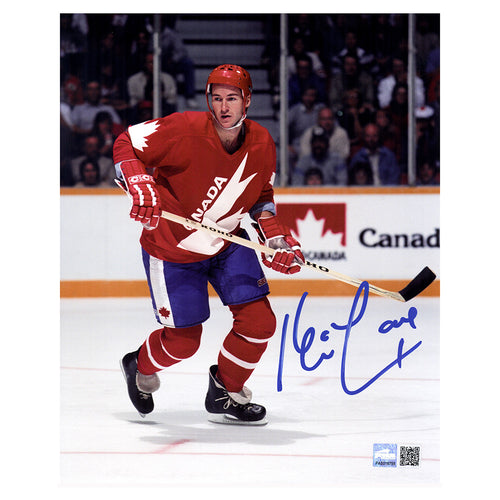 Kevin Lowe holding his stick and skating during a hockey game for Team Canada. He is wearing the red Team Canada hockey jersey with blue shorts and is looking to his right. Image is signed by Kevin Lowe with blue ink in the bottom right corner