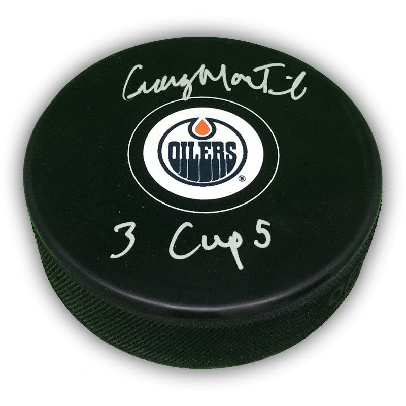 Black NHL hockey puck with Edmonton Oilers logo in the middle, signed by Craig MacTavish and inscribed "3 Cups"