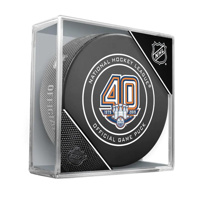 Black NHL hockey puck featuring 40th anniversary Edmonton Oilers logo design on front. Puck held in clear display case featuring corner designs featuring the NHL crest logo