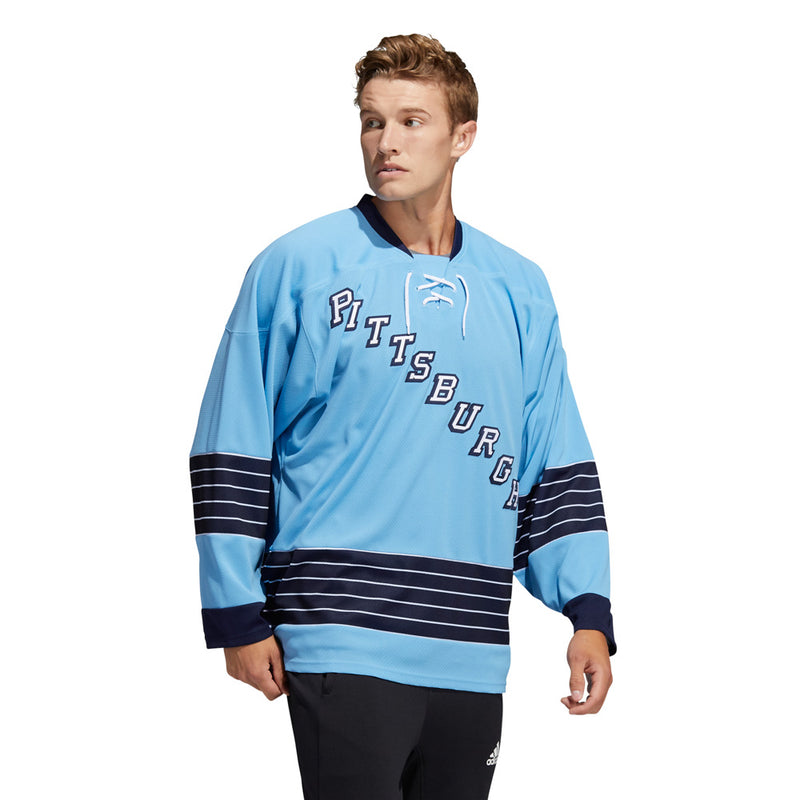 Model wearing the adidas vintage team classics 1967 Pittsburgh Penguins jersey, featuring blue and white striping on sleeves and lower hem. Model has short wavy blonde hair and he is looking to the right while walking