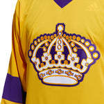 Front detail view of adidas Vintage team classics 1967 Los Angeles Kings jersey, featuring bold embroidered team logo on front chest and purple bands on sleeves and lower hem, and purple collar. Primary jersey collar is a bright sunshine yellow