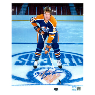 Signed photo of young Mark Messier posed on the ice with stick and puck. He is wearing the Edmonton Oilers royal blue jersey. Photo is signed near the bottom in blue ink. 