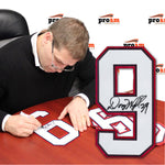 Photo of Doug Weight signing jersey numbers while seated at  a table, large signed number 9 is inset in the image 