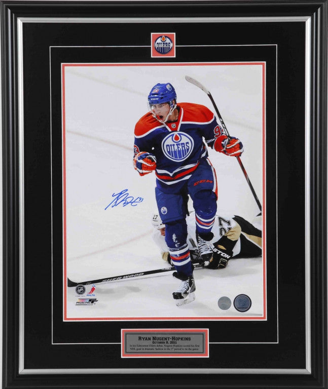 Autographed photo of Ryan Nugent-Hopkins during an Edmonton Oilers home game, opponent on ice behind him. Framed in black with silver and orange accents, inset Oilers crest at top and descriptive plaque at bottom 