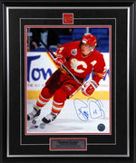 Theo Fleury of the Calgary Flames skating during a Calgary Flames NHL hockey game wearing red jersey with alternate captain's A. photo is signed in blue ink in the bottom right corner. Photo is framed with black frame, black mat with red accent, team pin and descriptive plate. 