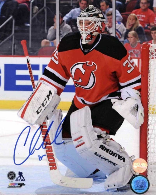 Corey Schneider in the net during a New Jersey Devels hockey game. He is wearing red Devils jersey with white goalie pads. The photo is signed in the bottom left corner using blue ink. 