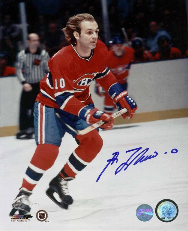 Guy Lafleur skating during a Montreal Canadiens hockey game. He is carrying his hockey stick and wearing red and blue jersey with no helmet. Photo is signed by Lafleur in blue ink. 