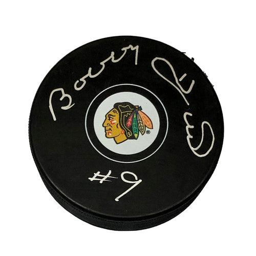 Black hockey puck with Chicago Blackhawks logo in the middle of the front. Puck is signed by Bobby Hull