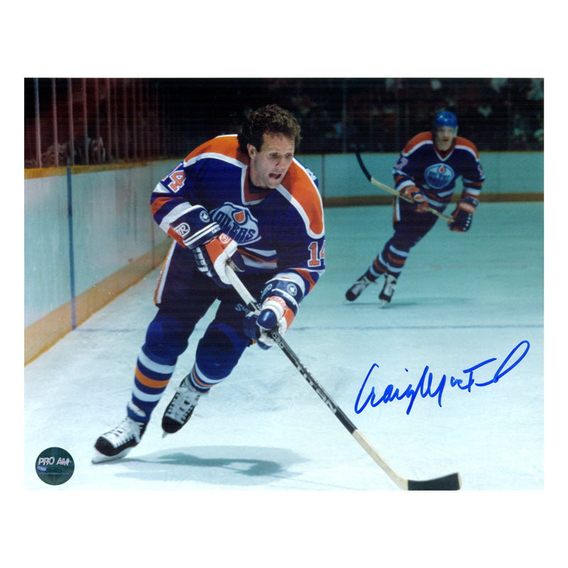 Photo of Craig MacTavish Edmonton Oilers skating during an NHL hockey game wile wearing royal blue jersey. Photo is signed in blue in in the lower right. 
