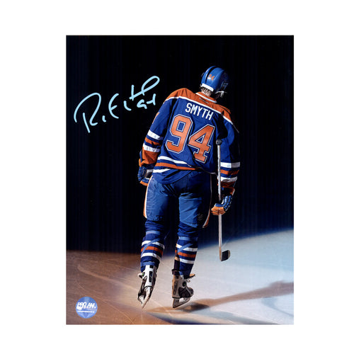 Photo of Edmonton Oilers Ryan Smyth skating away towards dark background, wearing royal blue jersey, during his last game with the Oilers before retirement. Photo is signed in light blue ink in the upper left.