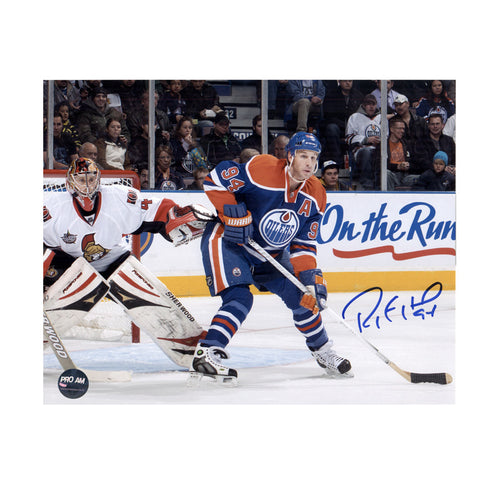 Photo of Edmonton Oilers Ryan Smyth in front of net and opposing team's goalie during an NHL hockey game, he is wearing royal blue jersey. Photo is signed with blue ink in the lower right corner. 