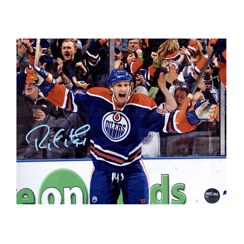 Ryan Smyth celebrating during an Edmonton Oilers NHL hockey game. He is wearing royal blue jersey. Image is signed on the left side in light blue ink. 