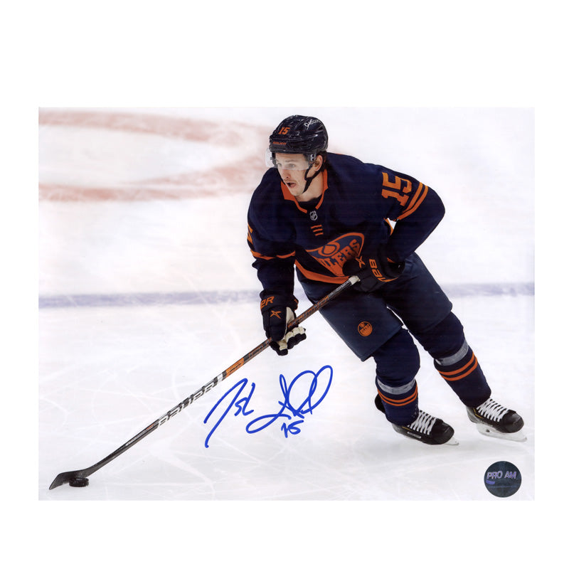 Photo of Edmonton Oilers Josh Archibald skating with puck during Oilers NHL game, wearing navy alternate jersey. Photo is signed near the bottom in dark blue ink. 