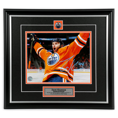 Photo of Edmonton Oiler Zack Kassian wearing orange jersey celebrating during an Oilers NHL hockey game. Photo is signed in light blue ink in the lower right. Photo is shown framed in black frames and mat with orange accents, team pin and description plate are inset. 