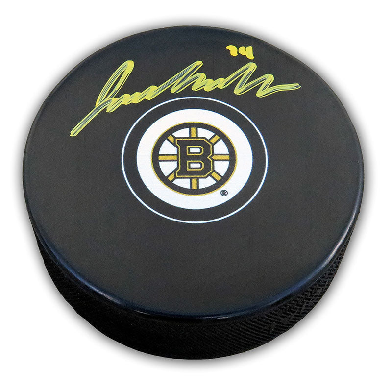 Black NHL hockey puck with Boston Bruins logo; puck has been signed by Jake Debrusk in yellow ink. 