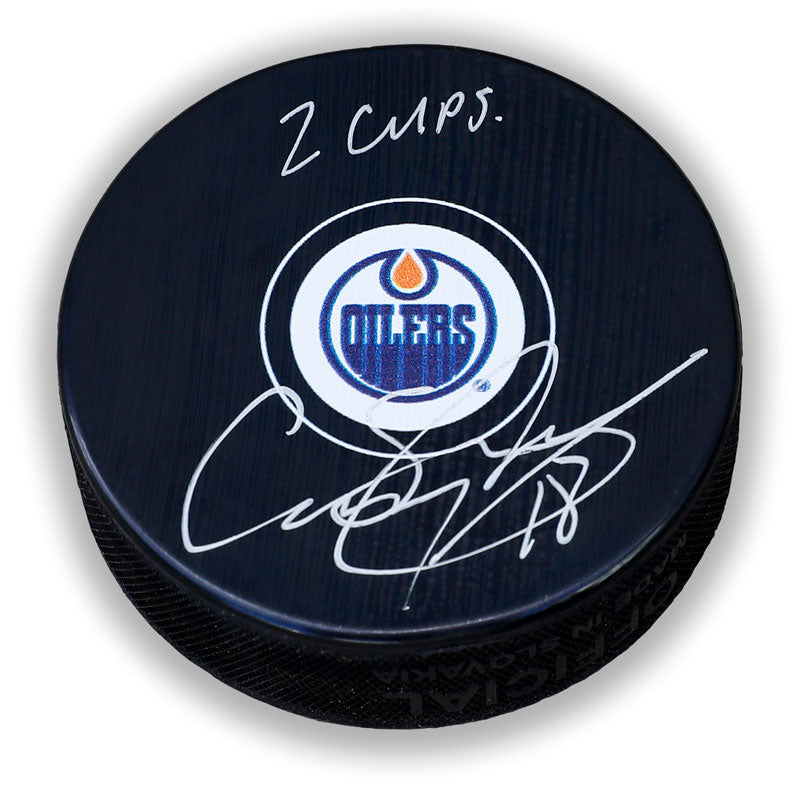 Black NHL hockey puck with Edmonton Oilers logo; signed by Craig Simpson with inscription "2 Cups"